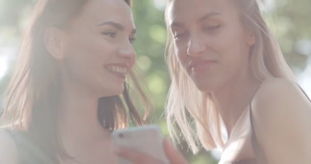 Twee tienermeisjes gebruik mobiele telefoon in een stadspark. — Stockvideo