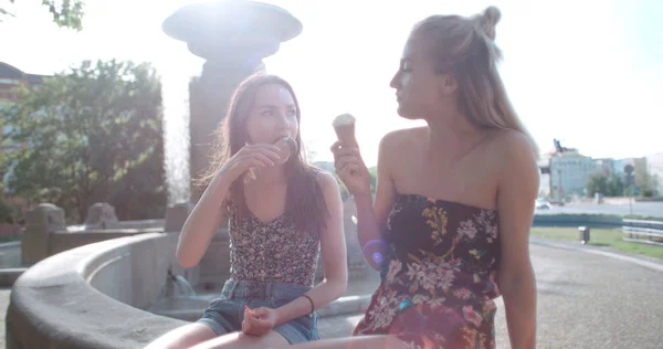 Two female friends eating ice cream and chatting in city. — Stock Photo, Image