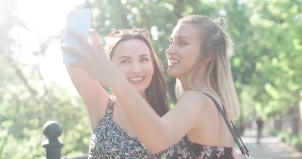 Dos hermosas adolescentes usando el teléfono en un parque de la ciudad . —  Fotos de Stock
