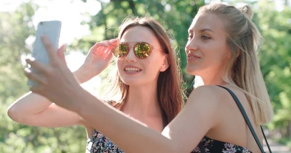 Dos hermosas adolescentes usando el teléfono en un parque de la ciudad . —  Fotos de Stock