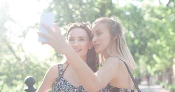 Dos hermosas adolescentes usando el teléfono en un parque de la ciudad . —  Fotos de Stock