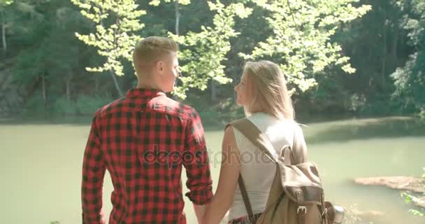 Rear view of hugging couple standing on a lake shore in a forest. — Stock Video