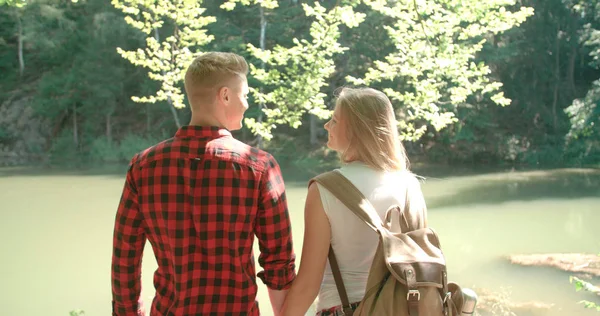 Vista trasera de la pareja abrazada de pie en una orilla del lago en un bosque . — Foto de Stock