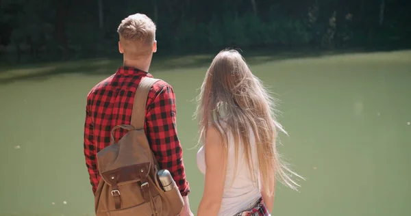 Vista trasera de la pareja abrazada de pie en una orilla del lago en un bosque . — Foto de Stock