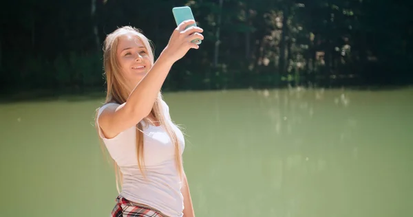 Mujer joven tomando una selfie por un teléfono inteligente en un bosque . —  Fotos de Stock
