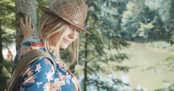 Şapka ve sırt çantası takmış bir ormandaki güzel beyaz kadın portresi. — Stok video