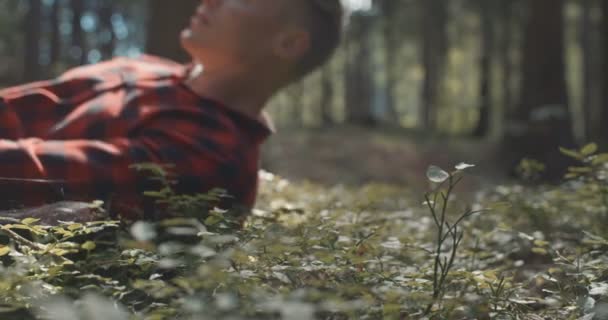 Mann im karierten Hemd ruht mit geschlossenen Augen im Wald. — Stockvideo