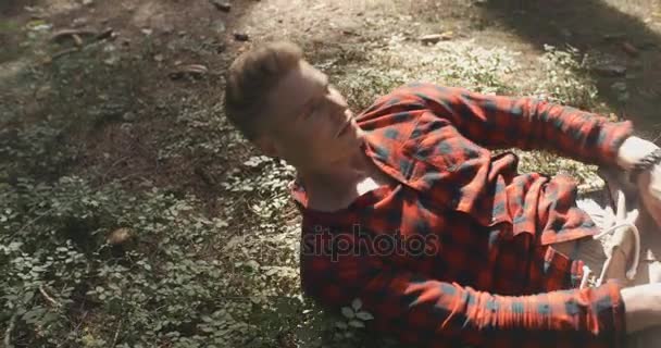 Man in checkered shirt resting with closed eyes in a forest. — Stock Video