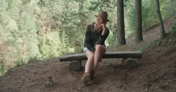 Porträt einer schönen kaukasischen Frau, die auf einer Holzbank im Wald sitzt. — Stockvideo