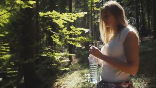 Молода жінка п'є воду на відкритому повітрі в сонячному парку або лісі . — стокове відео