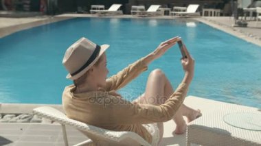 Selfie fotoğraf onu tatil sırasında yapma şapkalı güzel bir kadın. Yüzme Havuzu dinlenirken telefon kullanan genç kadın.