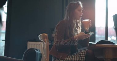 Restoranda oturan ve portakal suyu içme sırasında cep telefonu kısa mesaj yazarak neşeli bir genç kadının portresi.