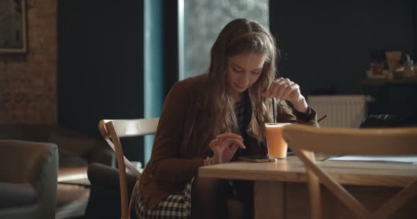一个欢快的年轻女子的肖像坐在餐厅和喝橙汁的手机上键入短信 — 图库视频影像