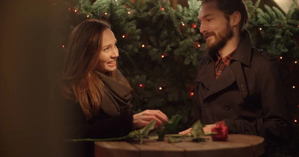 Young couple dating at night in the lights of the city street. Beautiful young couple talking by outdoors restaurant table.