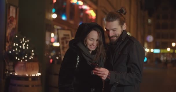若い幸せなカップルの夜のスマート フォンを使用して 美しいカップル オンライン モバイル アプリと思い出とソーシャル メディア上の写真を共有します — ストック動画