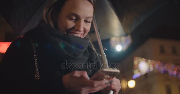 晚上在一个城市使用智能手机的年轻妇女 美丽的女人在城市晚上手持智能手机和短信 — 图库视频影像