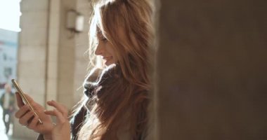 Telefon bir şehirde kullanan genç beyaz kadın. Güzel genç kadın telefonla güneşli gün boyunca yazarak.