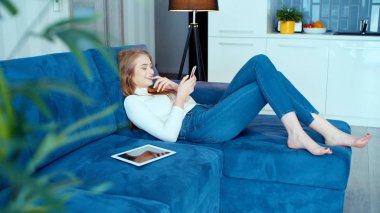 Evde kanepede otururken telefon kullanan genç gülümseyen kadın.