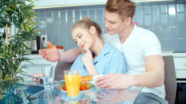 Genç çift mutfak masasında Kahvaltı yaparken dijital tablet kullanma.