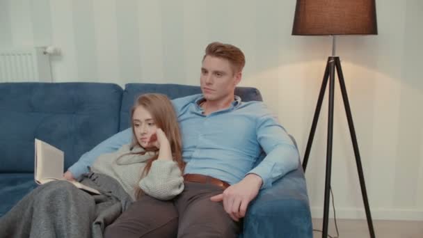 テレビを見て 本を読んでのソファの上に座って美しいカップル — ストック動画