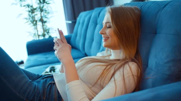 在家坐沙发的年轻微笑的妇女用电话 — 图库视频影像