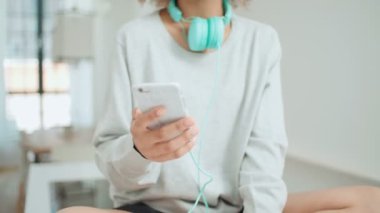 Müzik keyfi ve telefon tutarak mutlu ve neşeli genç kadın. Güzel genç afro Amerikalı kadın evde mutfak masasında oturan renkli kulaklıklarla.