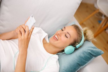 Evde akıllı telefonu ve kulaklığı olan genç bir kadın var..