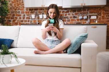 Evde akıllı telefon kullanan genç bir kadın..