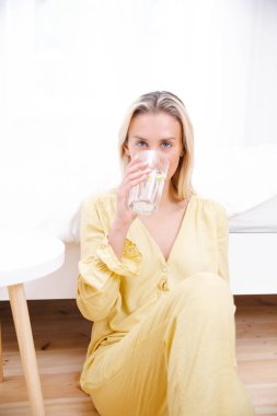 Genç bir kadın sabah bir bardak suyla yatağında oturuyor..