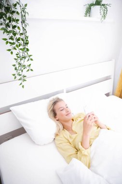 Güzel sarışın kadın pijama giyiyor. Yatak odasında telefon kullanıyor..