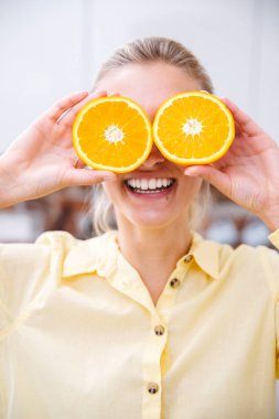 Komik ve neşeli genç kadın gözlerinin yanında portakal dilimleri tutarak ve gülümseyerek.