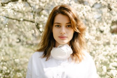 Antibakteriyel maske takan genç bir öğrenci bir parkta çiçeklerin arasında duruyor..