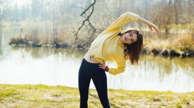 Genç esmer kadın şehir parkında esneme egzersizleri yapıyor.. 