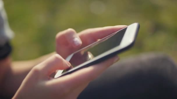 Gros plan des mains féminines à l'aide d'un téléphone intelligent dans un parc.