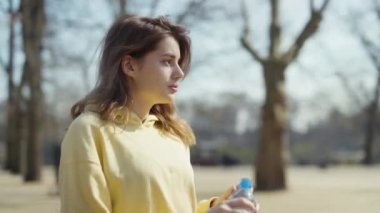 Genç esmer kadın parkta koştuktan sonra su içiyor..