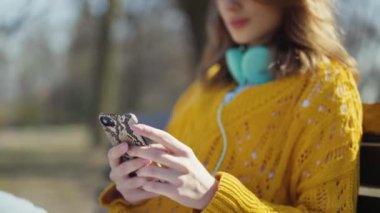 Şehir parkında telefon kullanan kulaklıklı genç bir kız..