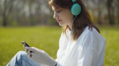 Şehir parkında telefon kullanan kulaklıklı genç bir kız..