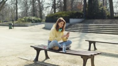Şehir parkında telefon kullanan kulaklıklı genç bir kız..