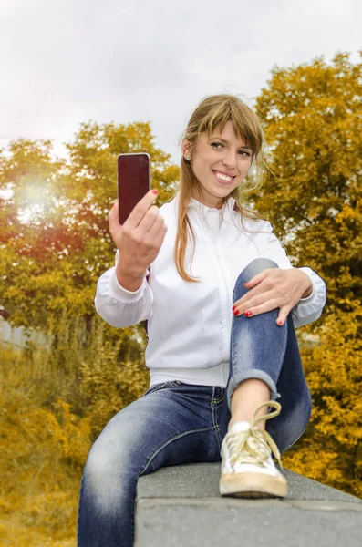 Дівчина з телефоном в парку робить селфі — стокове фото