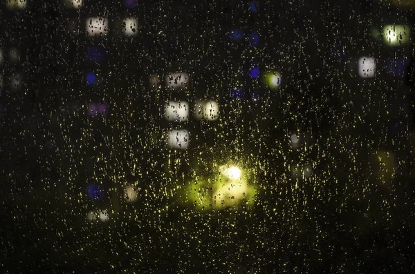 Druppels regen op het venster op de achtergrond van de bokeh van de nacht — Stockfoto