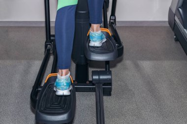 Mavi spor ayakkabılı kadın bacakları stepper simülatöründe çalışıyor.