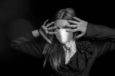 Tıbbi maske, koronavirüs ve diğer virüslere karşı koruma. Siyah takım elbiseli kadın siyah arka plandaki kameraya bakıyor.