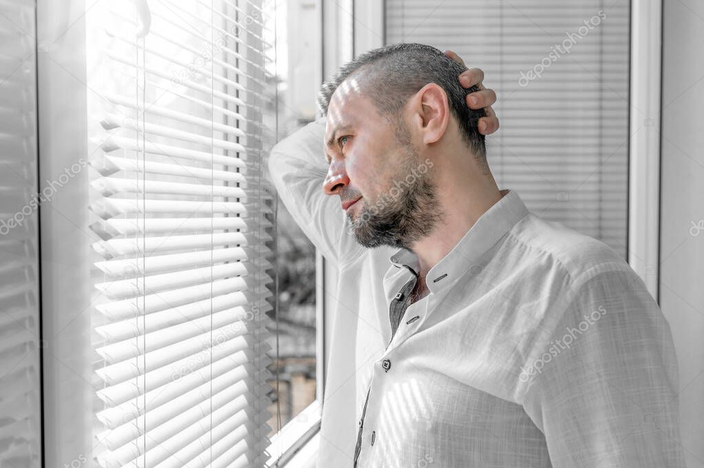 Man in isolation looking through window blinds. Coronavirus outbreak. Man looks at a sunny street through the window blinds