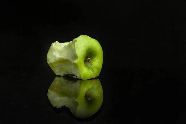 Egy Zöld Alma Csonkja Fekete Alapon Tükröződve — Stock Fotó