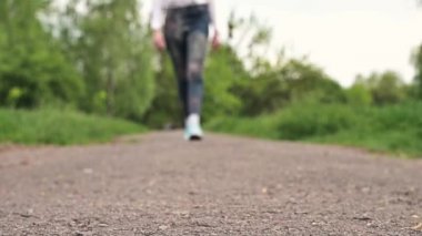 Spor ayakkabılı kadın toprak yolda yürüyor. Kot ve spor ayakkabı giymiş bir kız parkta yürüyor..