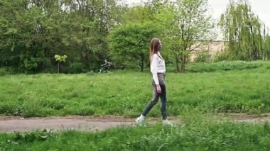 Spor ayakkabılı kadın toprak yolda yürüyor. Kot ve spor ayakkabı giymiş bir kız parkta yürüyor..