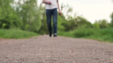 Spor ayakkabılı adam toprak yolda yürüyor. Kot pantolon ve spor ayakkabı giymiş bir çocuk parkta yürüyor. Kapalı bacaklar, yürüyen bir adam.