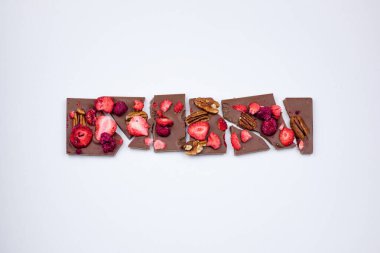 Beyaz arka planda fındık, kurutulmuş çilek ve ahududu olan kırık bir çikolata..