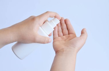 Çocuk beyaz arka planda antiseptikle elleri dezenfekte eder. Çerçeveye el at. Çocuklar ellerini yıkamak için alkol püskürtüyor.