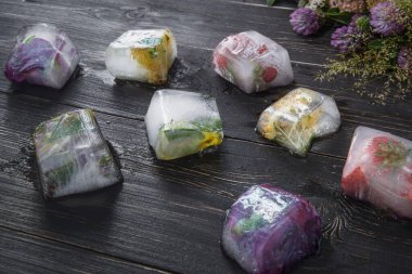 Şifalı bitkilerle dolu buz küpleri yonca çiçekli ahşap bir masanın arka planında.